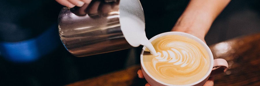 Ženské ruky tvoriace latte art z napeneného mlieka do cappuccina v ružovej šálke