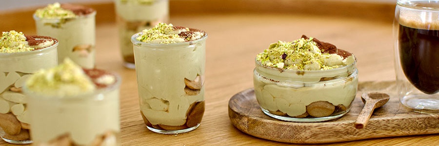 Pistáciové tiramisu v sklenenej nádobe na drevenom stole pri káve.