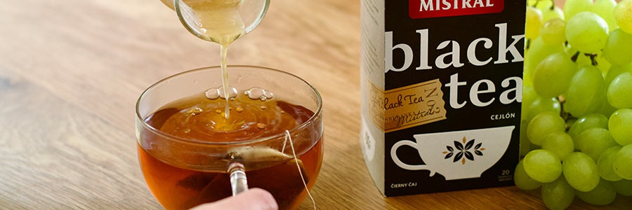 Žena leje domáci hroznový sirup do čierneho čaju Mistral na drevenom stole