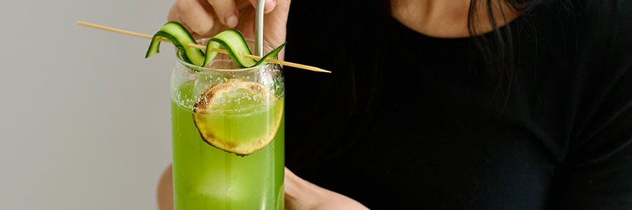 Žena pije domácu uhorkovú limonádu s ľadom, citrónom a ozdobou z čerstvej uhorky