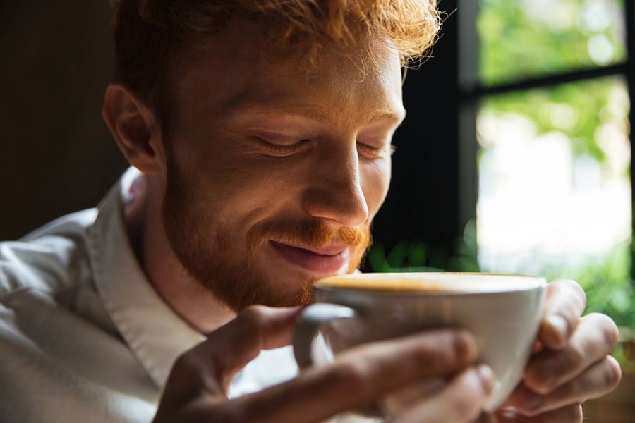 Muž si vychutnáva vôňu cappuccina z bielej šálky