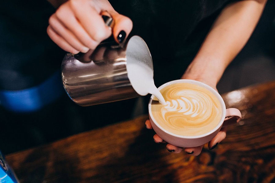 Ženské ruky tvoriace latte art z napeneného mlieka do cappuccina v ružovej šálke