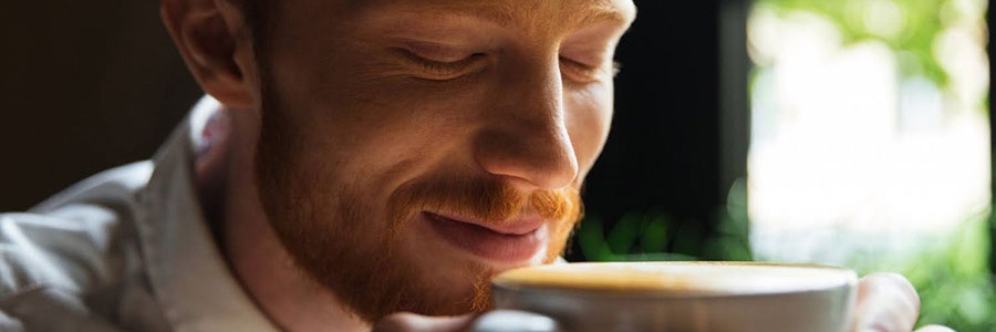 Muž si vychutnáva vôňu cappuccina z bielej šálky