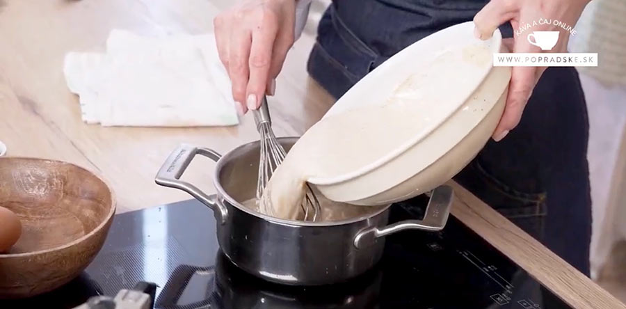 Ženské ruky prilievajú horúce mlieko za stáleho miešania do sivého hrnca