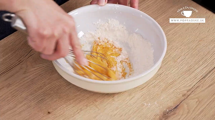 Ženské ruky miešajú žĺtka s vanilkovou pastou v bielej miske na kávový krém