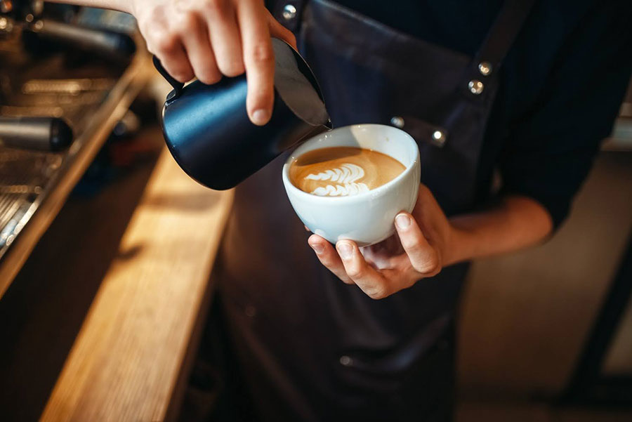 Barista pripravuje cappuccino vo fáze nalievania mlieka v bielej šálke