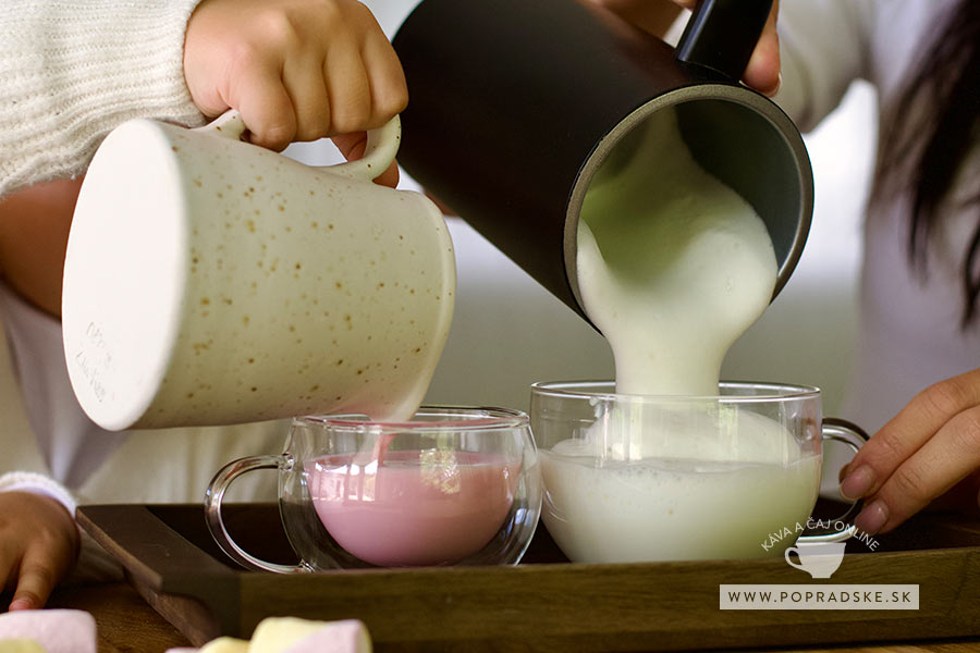Mama a dieťa si štrngajú sklenenými šálkami, dospelý drží cappuccino s mliečnou penou a dieťa ružové jahodové babyccino zdobené sušeným ovocím
