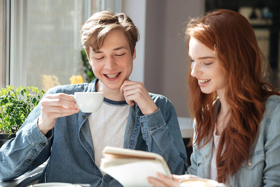 Dvaja mladí ľudia sa rozprávajú pri šálke kávy pri okne a listujú v zápisníku, vychutnávajú si prestávku Fika na kávu